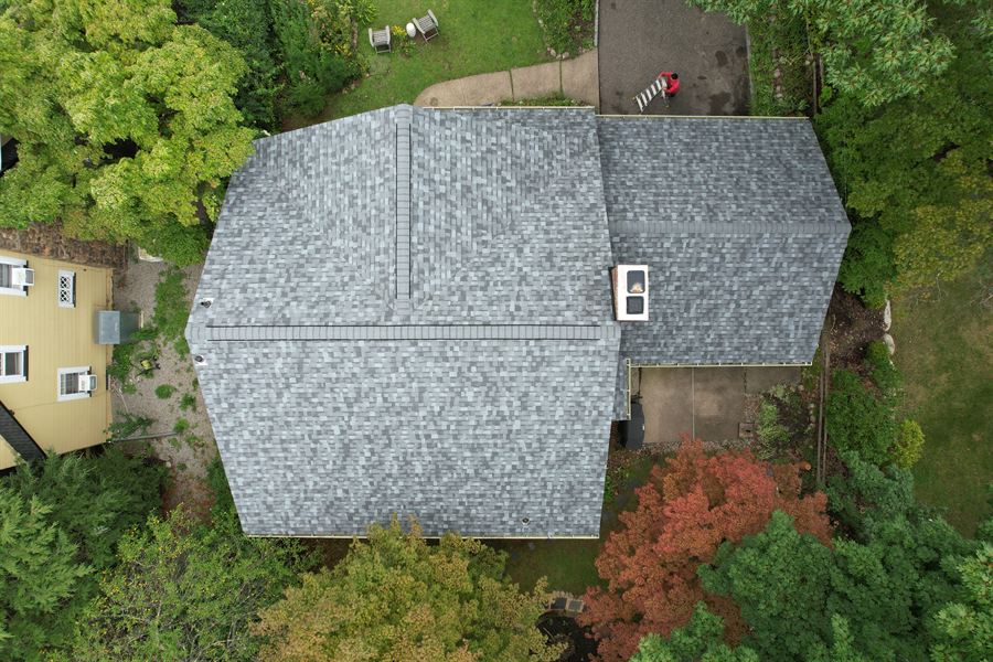 Top-down drone view of a finished gray shingle roof with new ridge vent and skylight